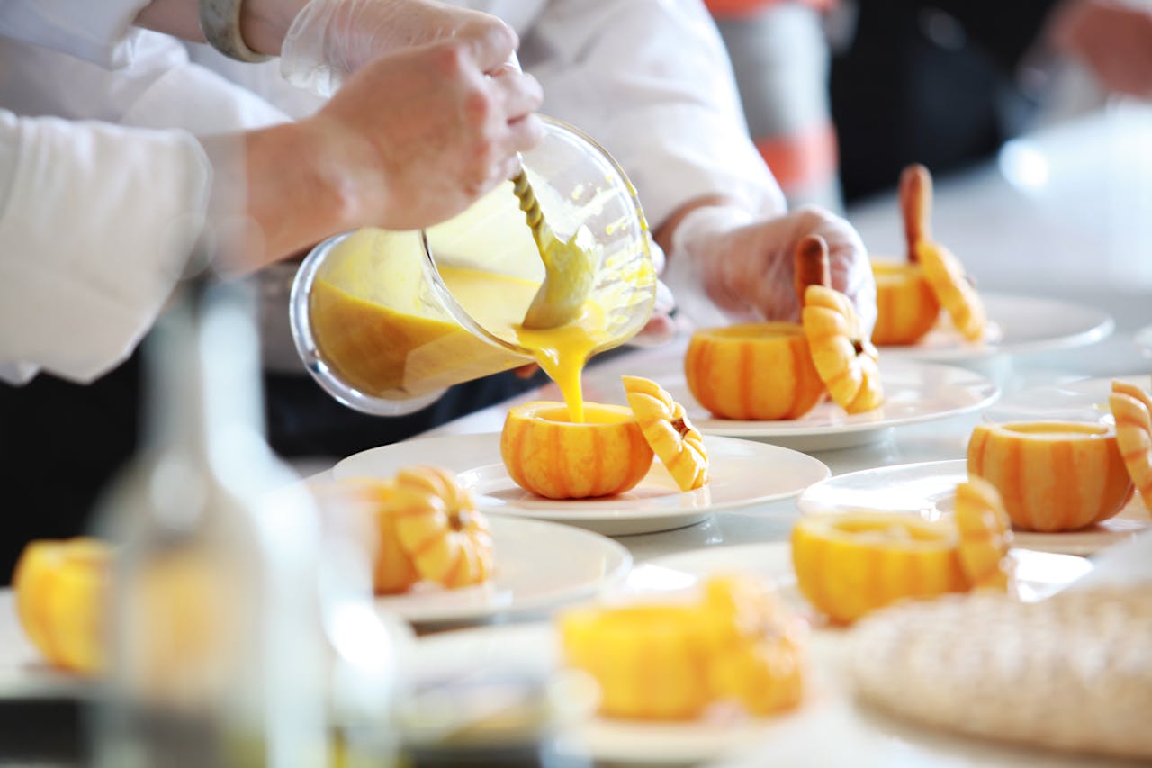 about-02 Chef performing culinary artistry by pouring vibrant pumpkin soup in decorative pumpkins.